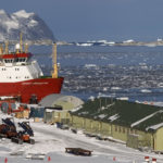 A landscape of an Antarctic base with a large ship docked nearby