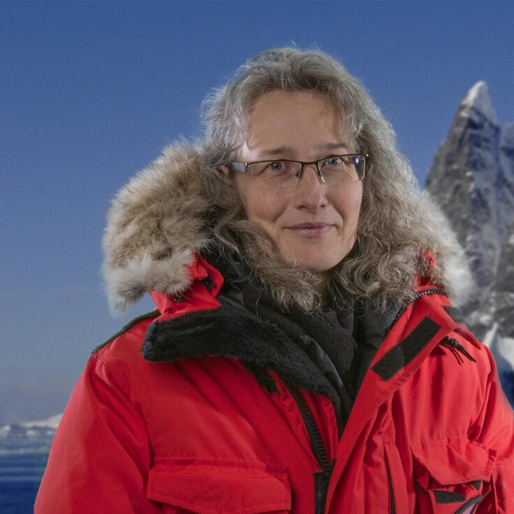 Beatrix Schlarb-Ridley, a middle aged white woman, stands in a hooded polar coat in front of a snowy landscape.
