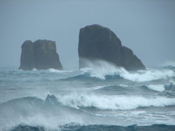 A man riding a wave on top of haystack rock.