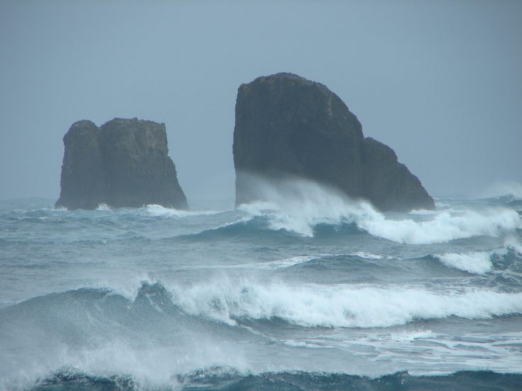 A man riding a wave on top of haystack rock.