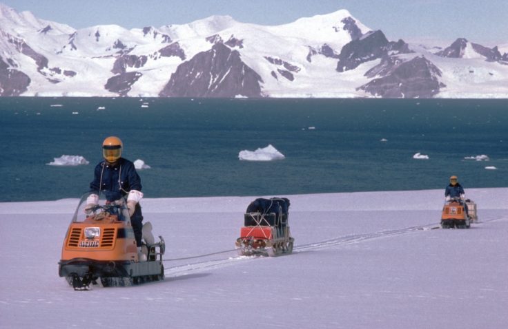 A man riding a skidoo down a snow covered mountain.