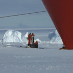 People working on the sea ice next to the hull of a large boat