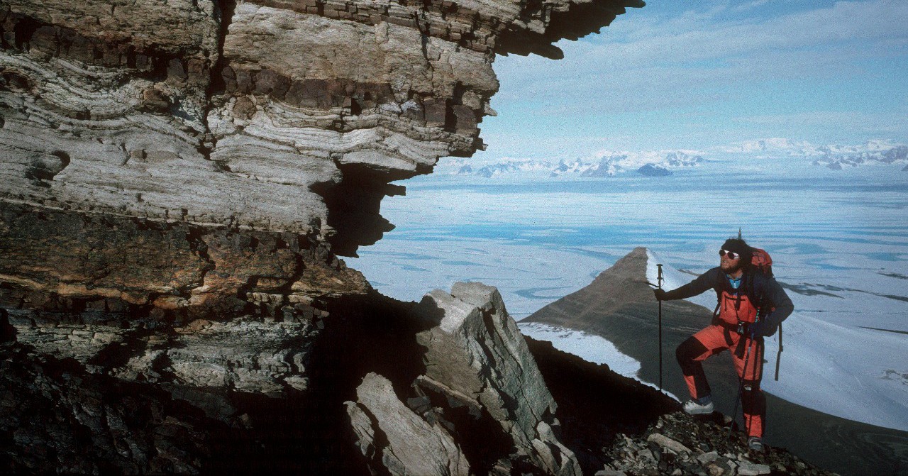 A man standing in front of a large rock next to water.
