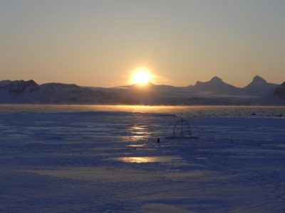 A sunset over a body of water with a mountain in the background.