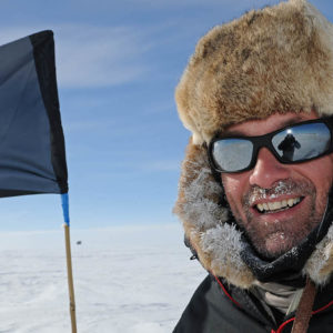 A man wearing cold weather clothing in front of a marker flag on the ice