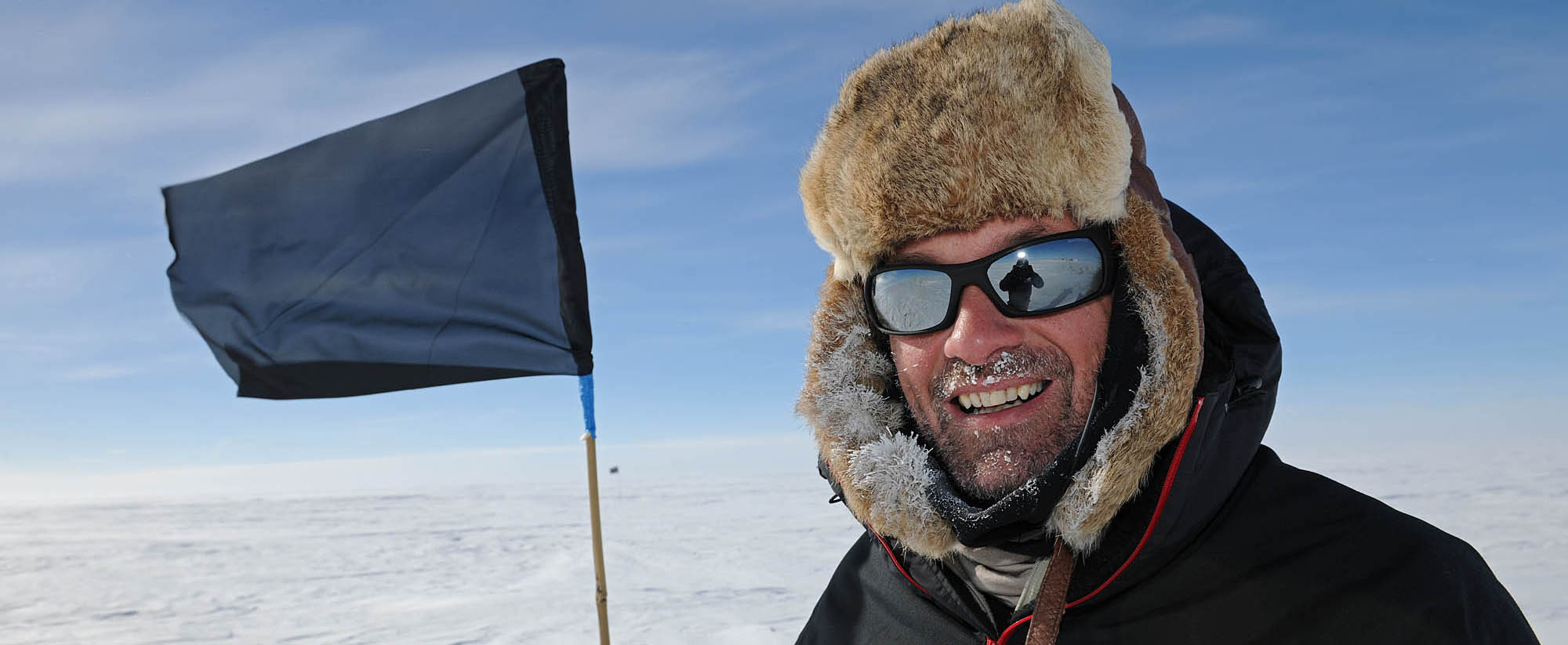 A man wearing cold weather clothing in front of a marker flag on the ice