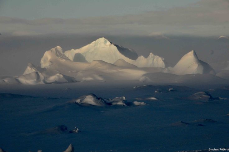 A group of clouds in the sky over a snow covered mountain.