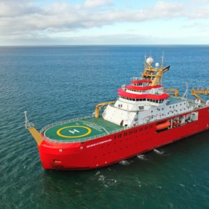 A large red ship with a green deck, sideways on, in the ocean