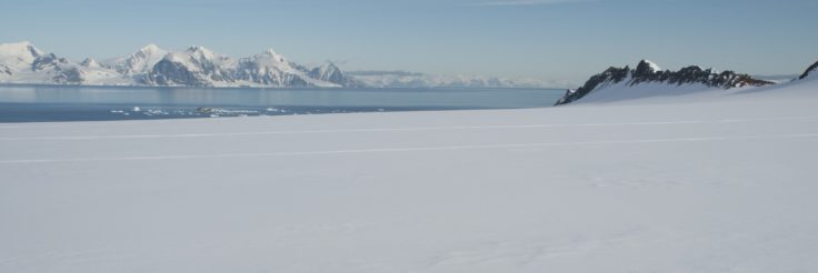 A snowy landscape with the sea in the background