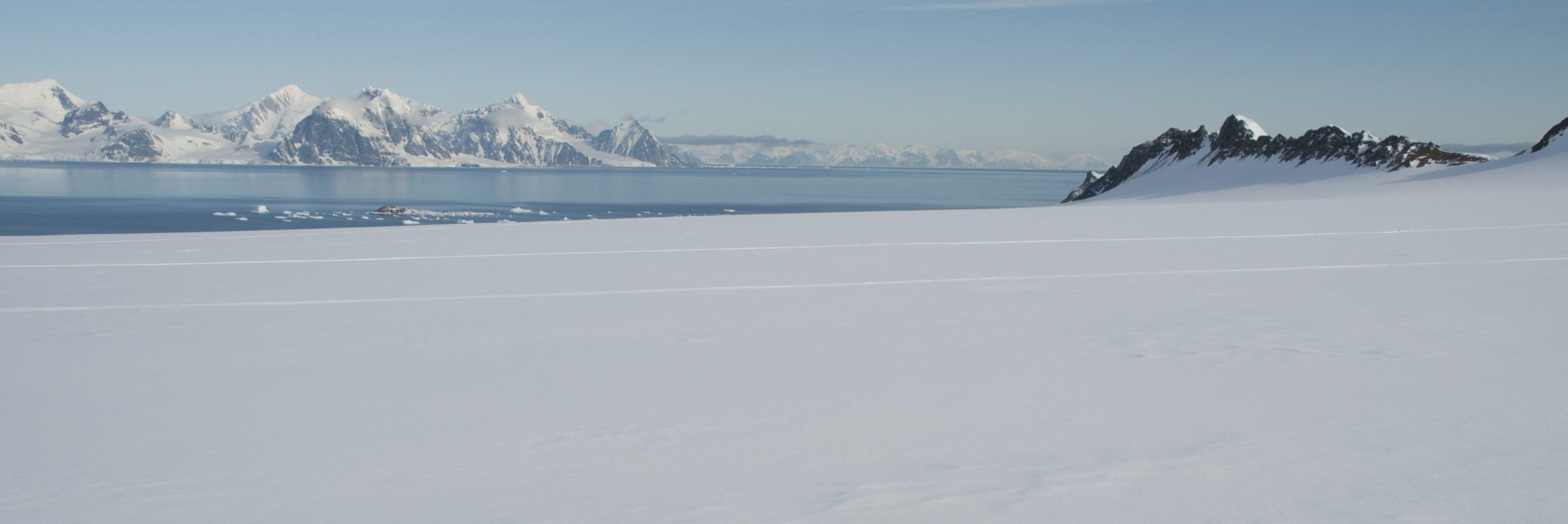 A snowy landscape with the sea in the background