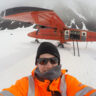 A man sitting on top of a snow covered mountain in front of a plane
