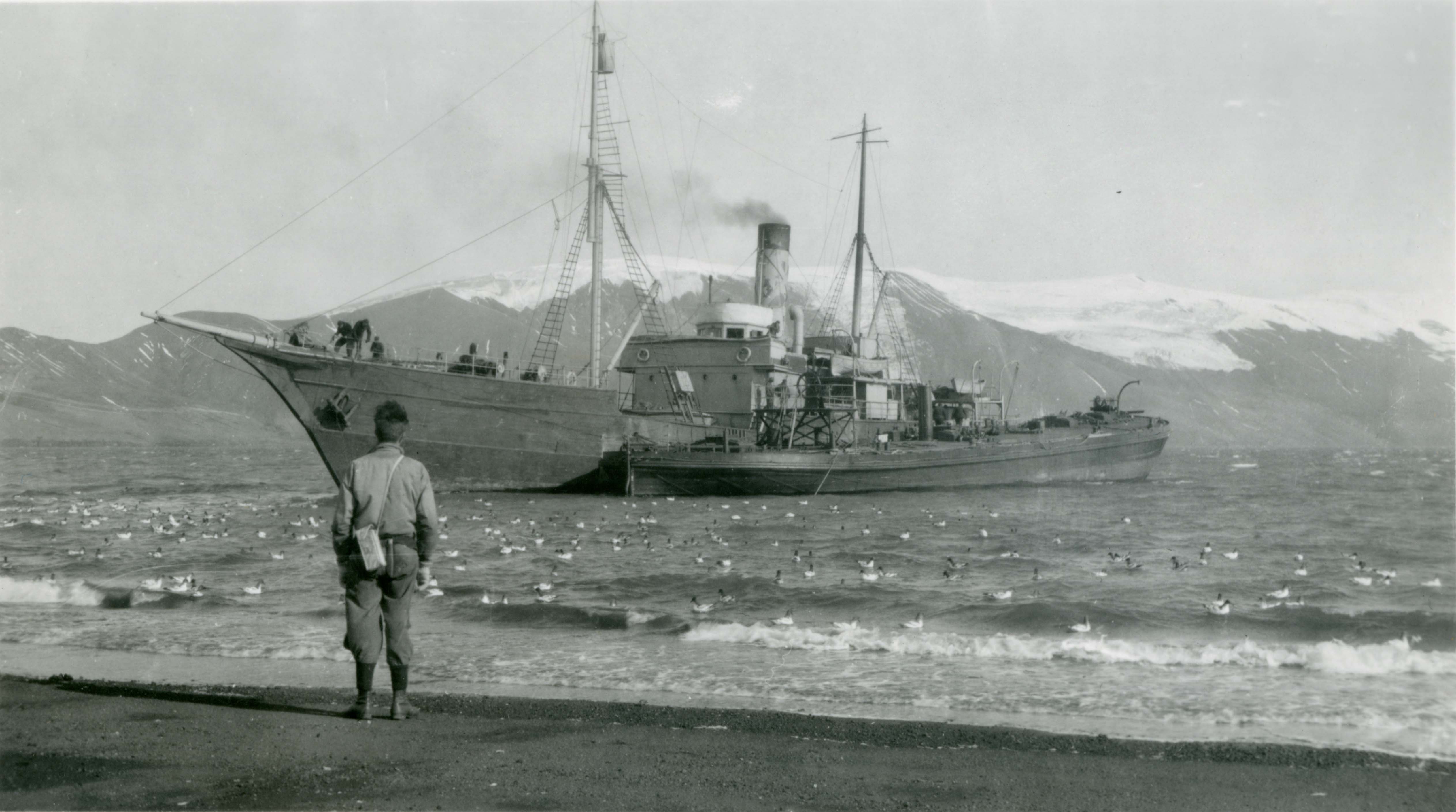 A person standing in front of a large ship in a body of water. Deception Island 1945