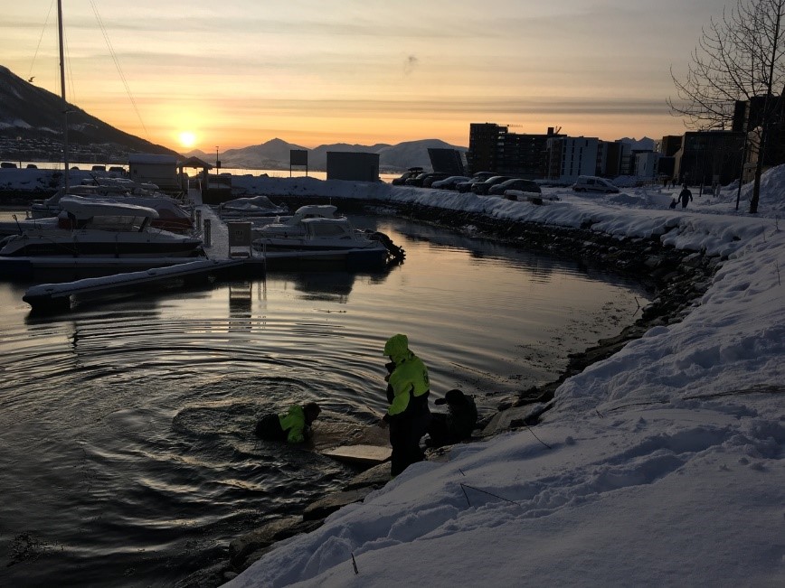 A sunset over a body of water with buildings in the snow.