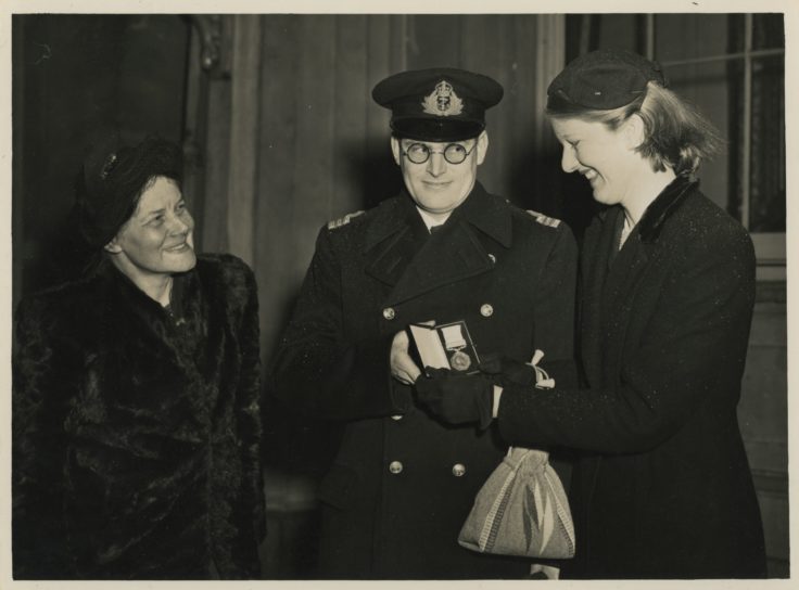 A black and white photo of a man in uniform flanked by two women
