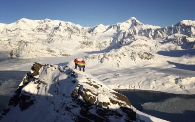 People on a snowy mountain range holding a rainbow flag