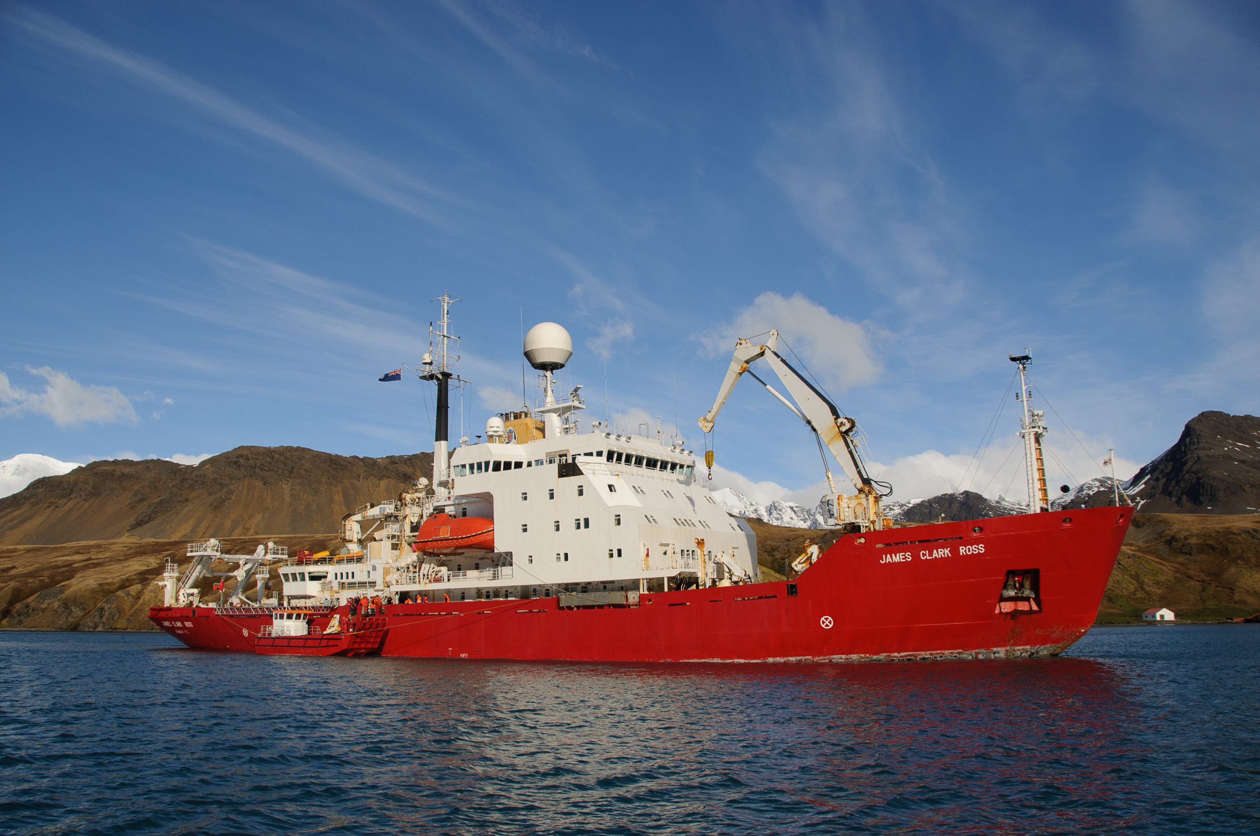 Large red ship in a body of water, with hills behind