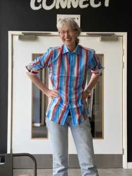 Tall female smiling standing in front of a wall wearing the Climate Code shirt, designed in collaboration with the British Antarctic Survey