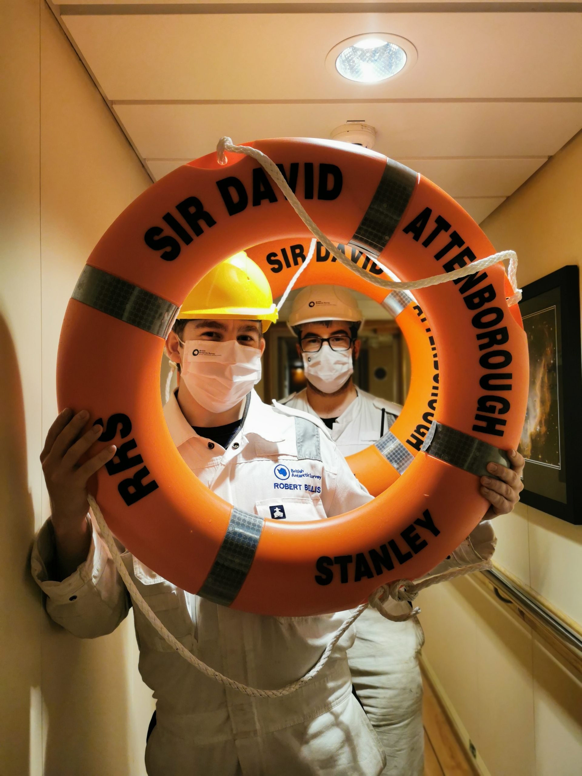 Two men in hard hats poke their faces through an orange life ring