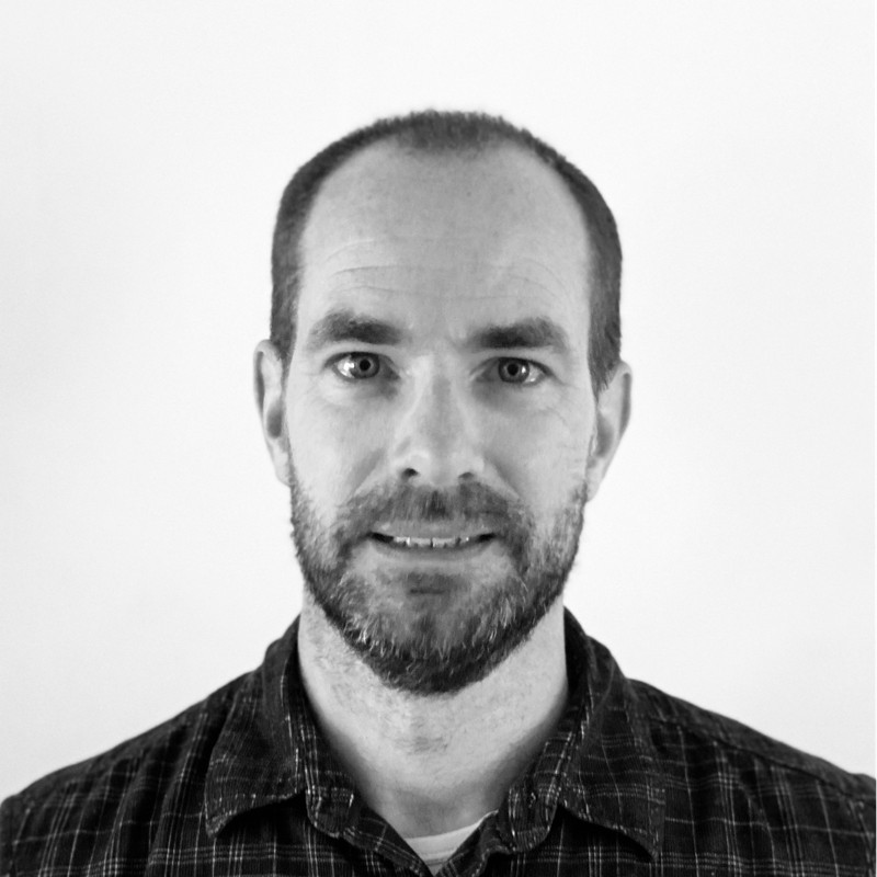 A man with a beard and checked shirt smiling at the camera