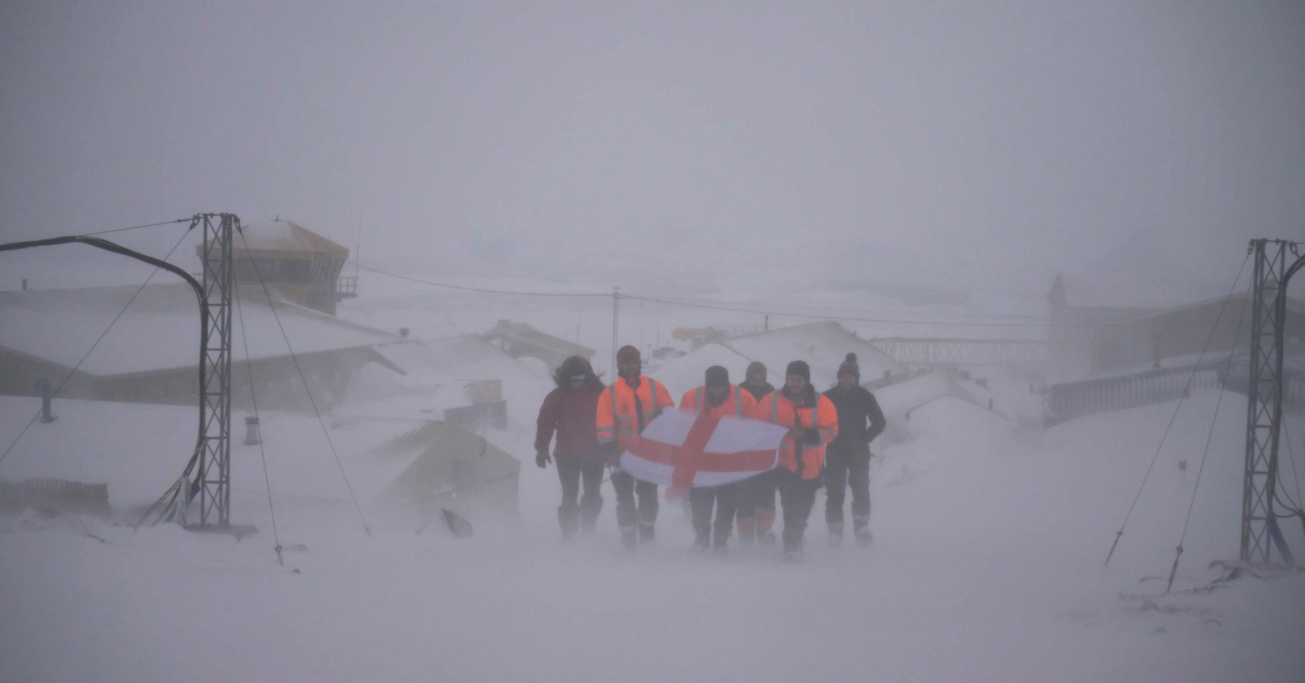 A group of people walking across snow covered ground, holding a flag