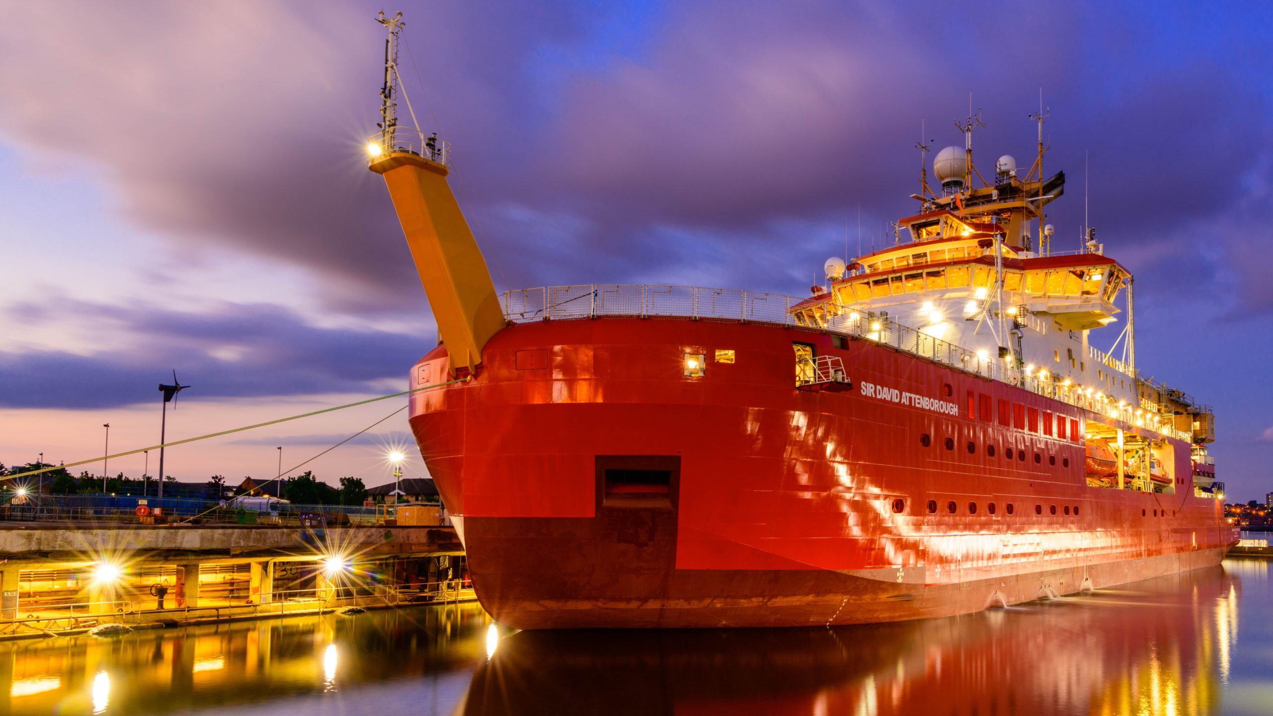 A large red ship in water. It is dark and the ship is lit up.