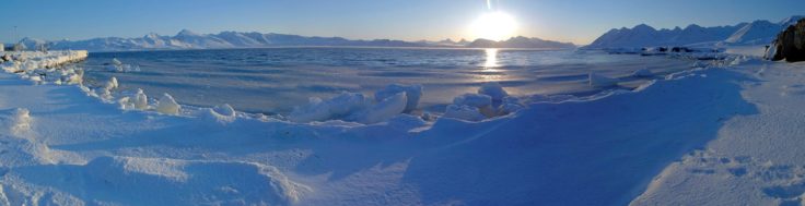 A body of water surrounded by ice with a mountain in the background