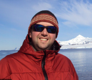 A man wearing sunglasses and standing next to a body of water