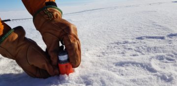 A person inserting a seismic node in the snow in Antarctica