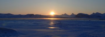 A sunset over a body of water with a mountain in the background