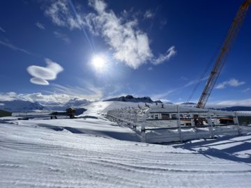 frame of new building being built in antarctica with snow in foreground and a mountain ridge in the background on a sunny day with a red crane to the right of the building
