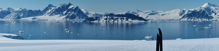 Skis in snow with body of water against snow covered mountains