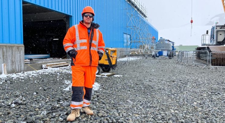 A man in high-visibility clothing standing next to a blue building