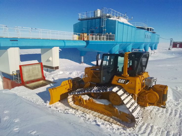 A CAT dozer is parked in front of a red hatch which is flush with the snow line. 