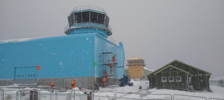 A blue building with a tower on the roof and snow on the ground