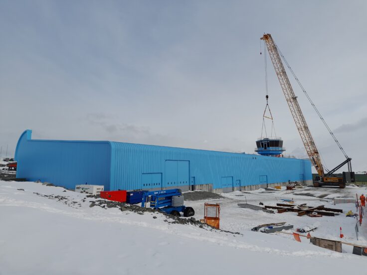 A blue building in the snow with a yellow construction crane beside it