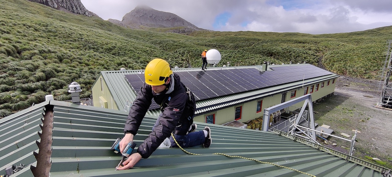 A person drilling a hole in a roof with green mountains behind