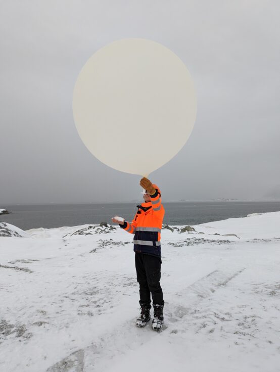A woman holding a large weather balloon in the snow