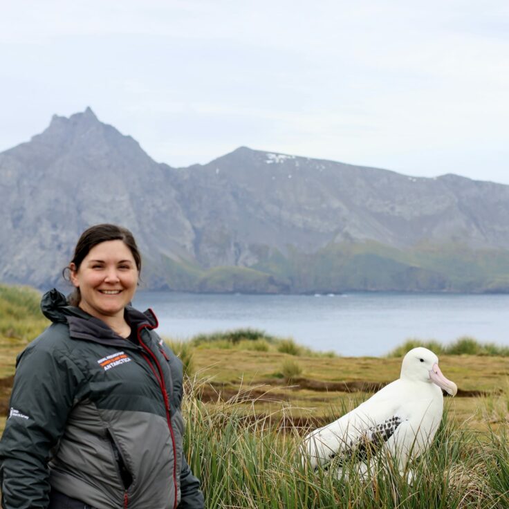 A man standing in front of a lake with a mountain in the background