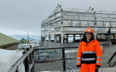 A woman wearing bright orange protective clothing standing on a construction site in snowy weather