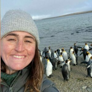 A woman on an beach with penguins behind her.