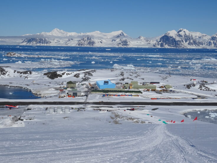 A large blue building in a snowy and icy landscape with white mountains in the background.