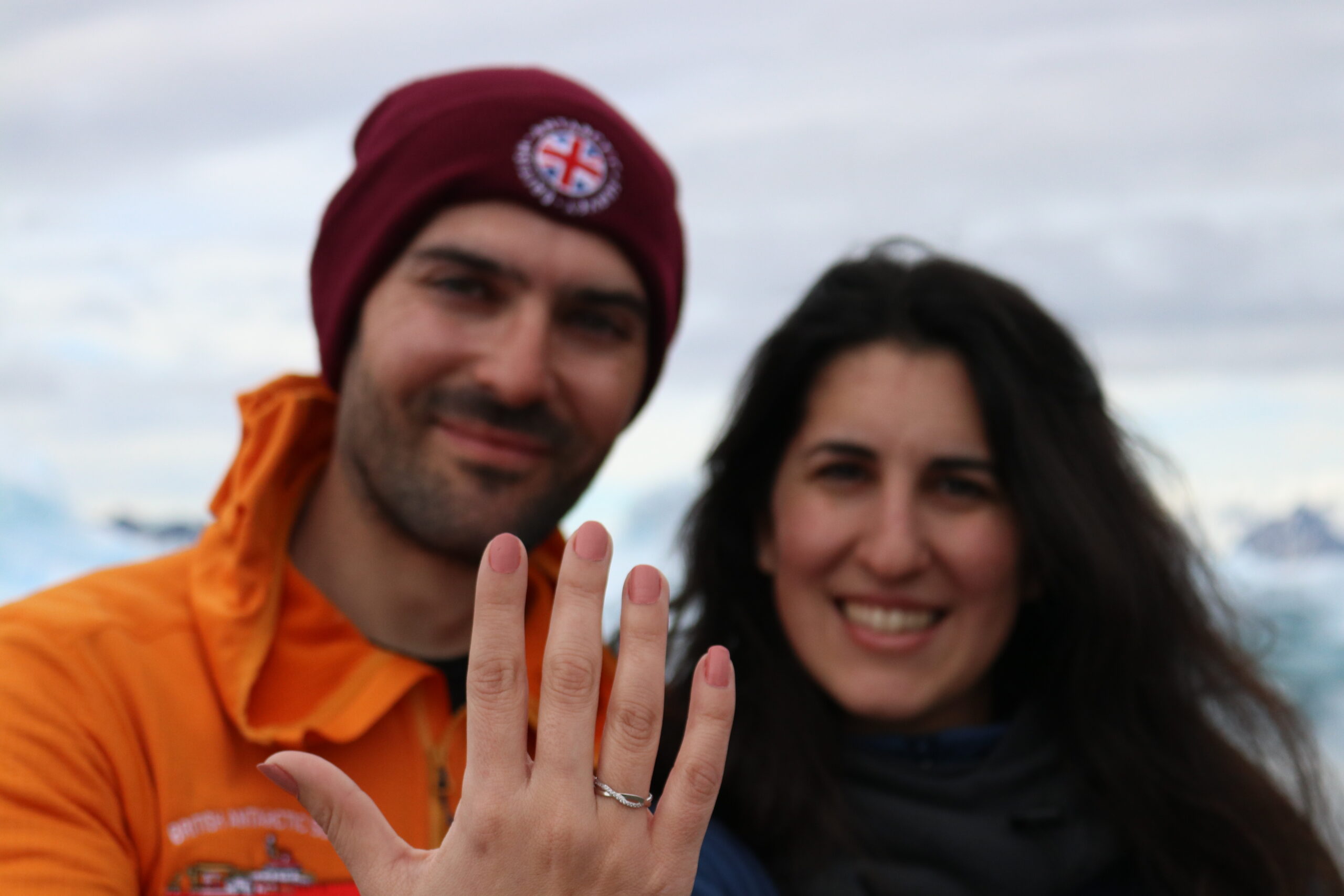 A smiling man and a woman holding up a hand to display an engagement ring