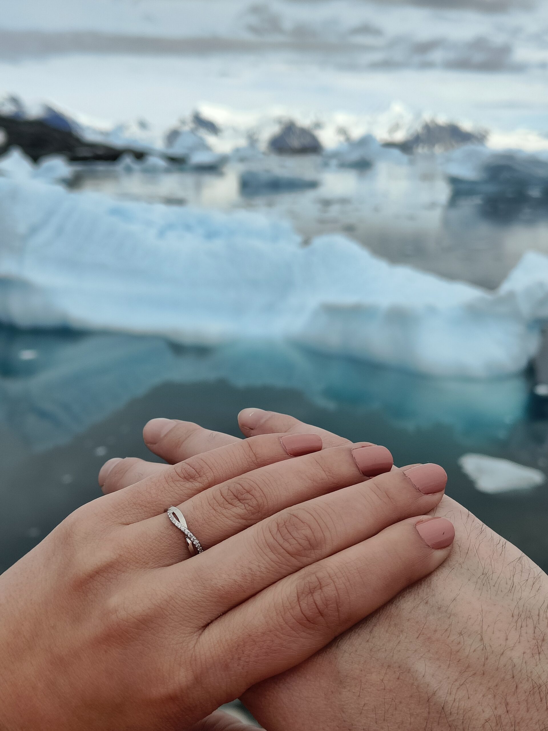 A hand with an engagement ring on a finger crossing over the top of another hand with icy mountains in the background