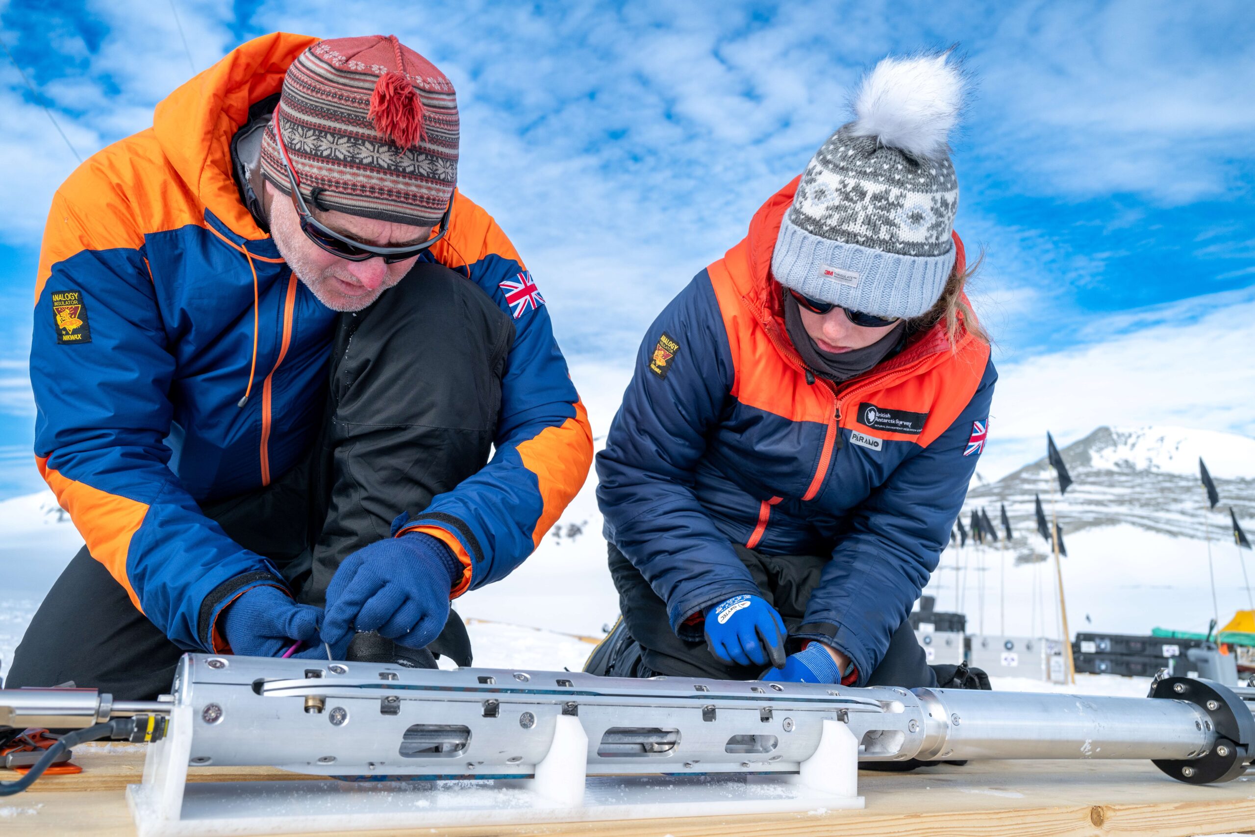 Two people hunched over an ice core drill.