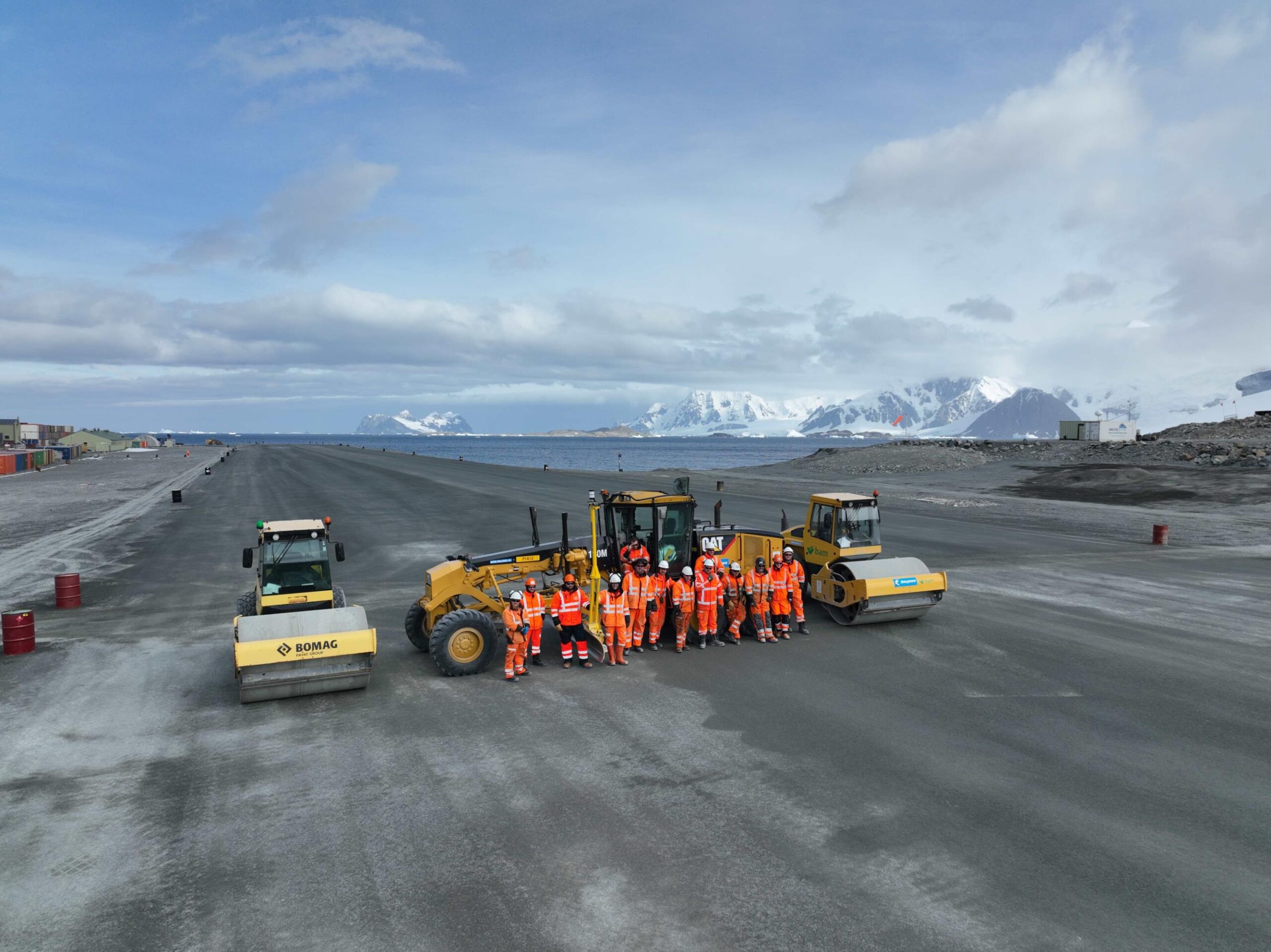 A group of construction workers standing on a runway with snowy mountains in the background.