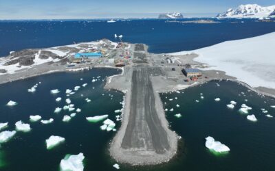 view of a runway from the air with icy waters and snowy mountain surrounding the runway.