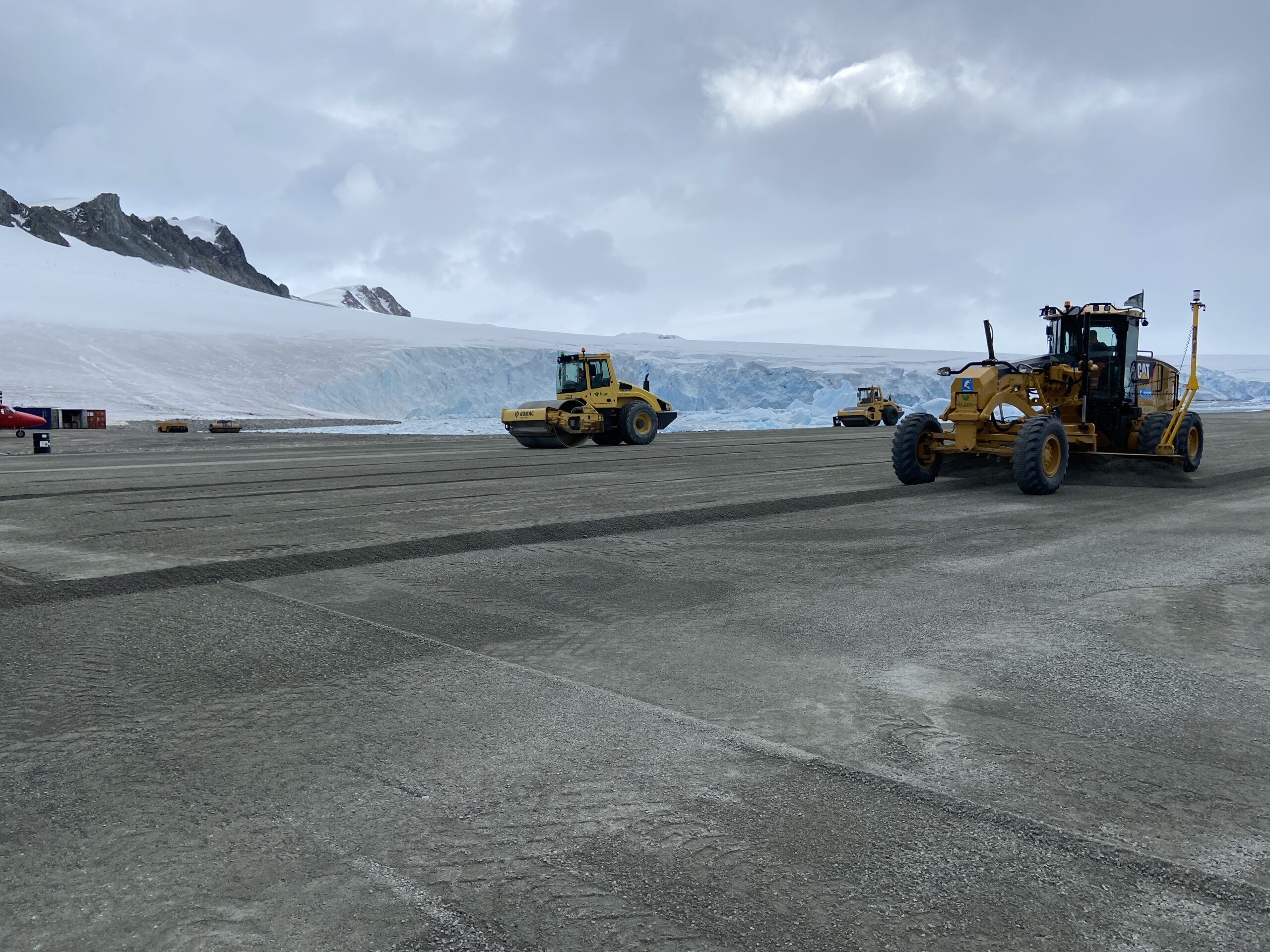Construction vehicles on a runway surface with ice in the background.