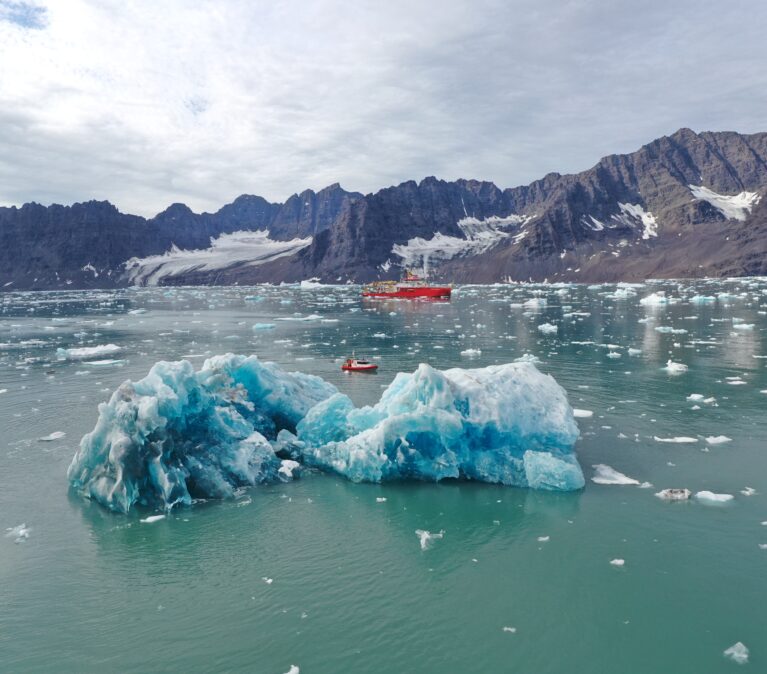 The RRS Sir David Attenborough sailing behind an Iceberg in Greenland