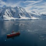 A ship in a Greenlandic fjord with a snow-capped mountain behind
