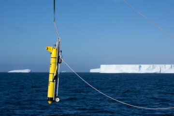 A long, thin yellow ocean glider dangles from a wire above the ocean